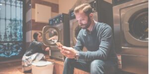 man sitting in laundromat looking at phone