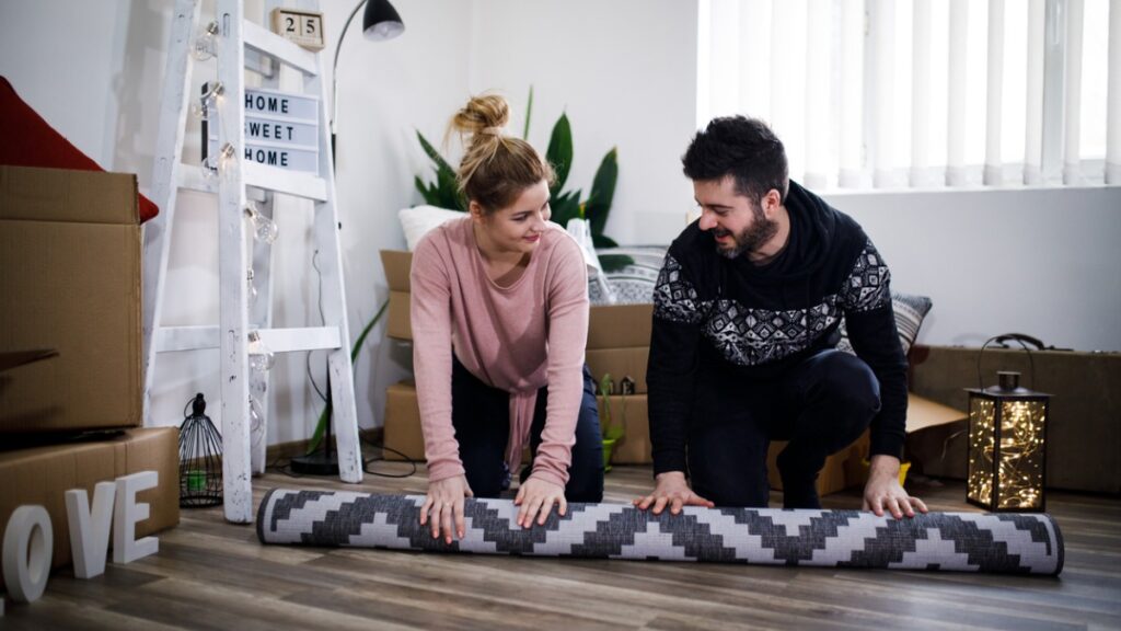 couple unrolling carpet in their new apartment