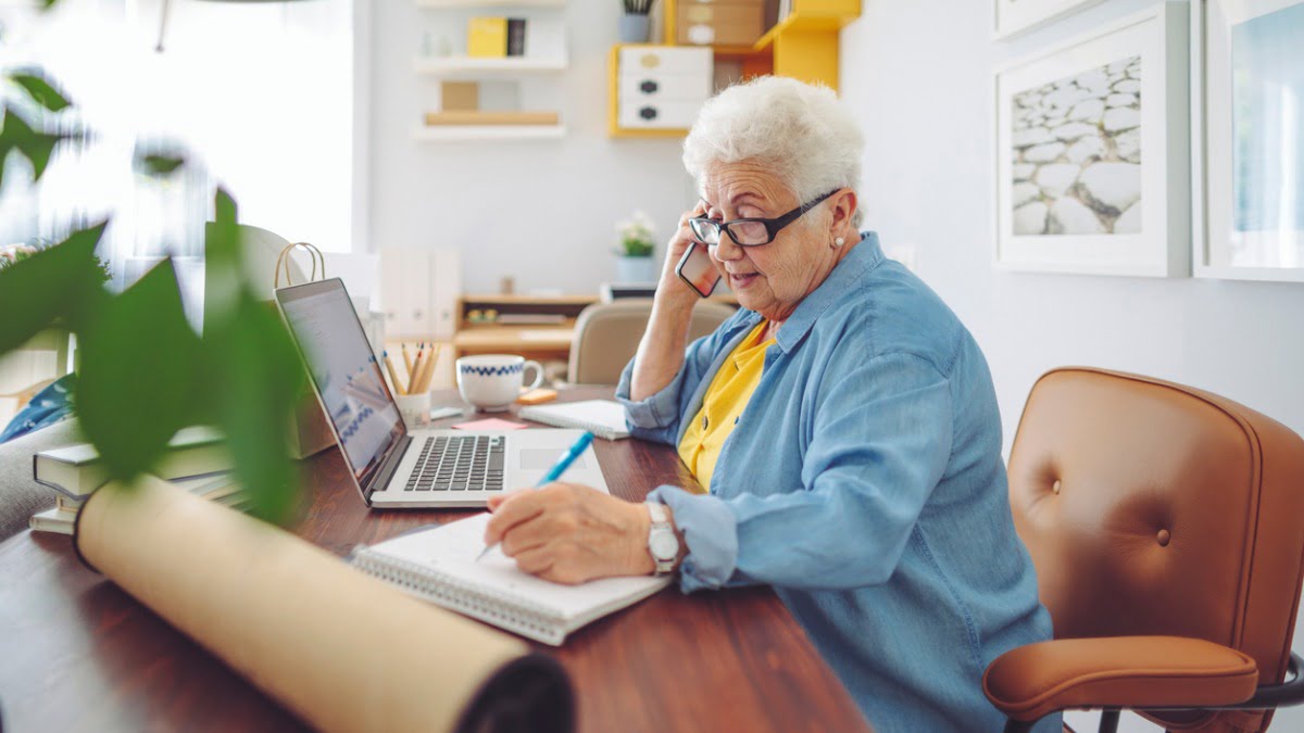 older woman on phone working at her laptop