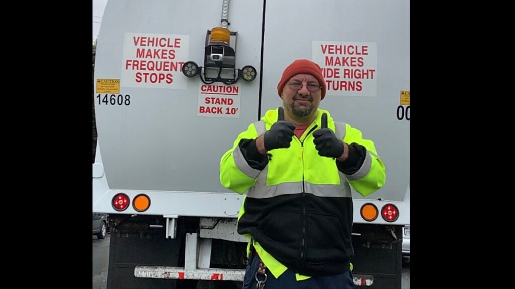 garbage man giving two thumbs up behind garbage truck