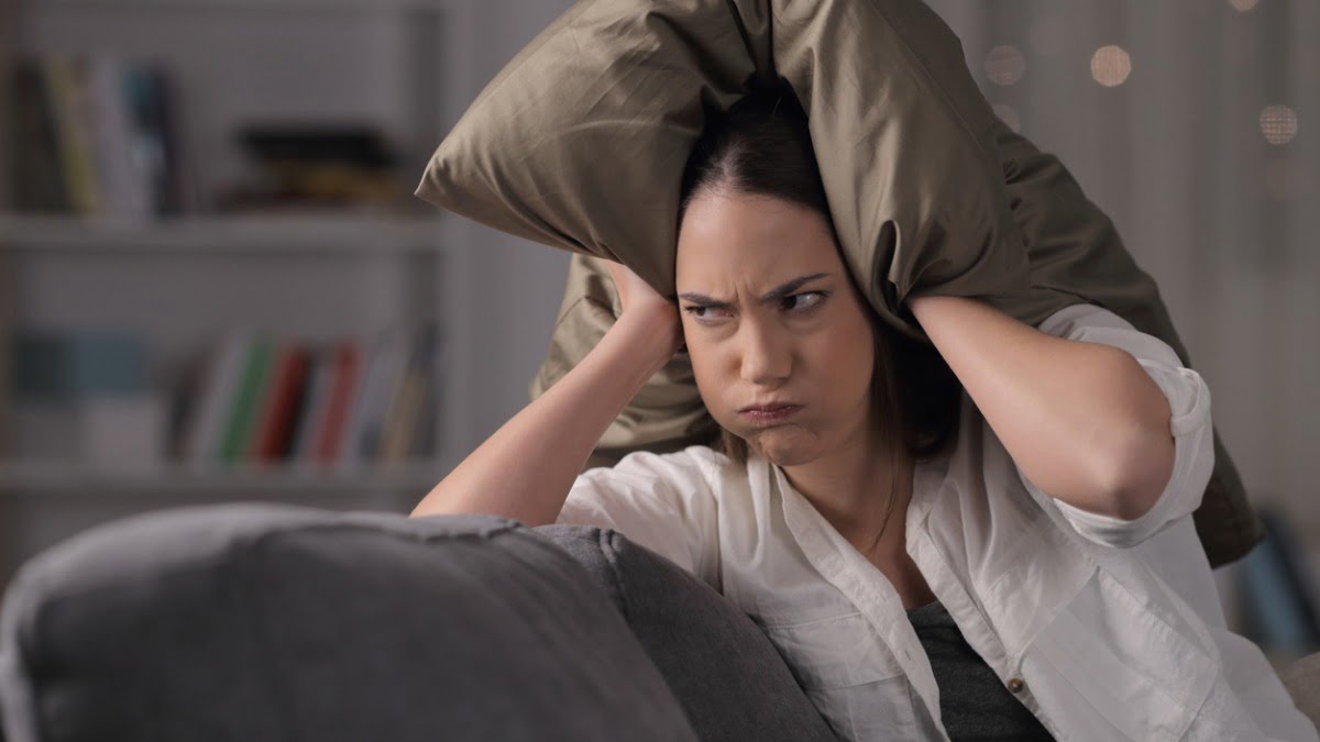 woman looking frustrated holding pillow over her ears