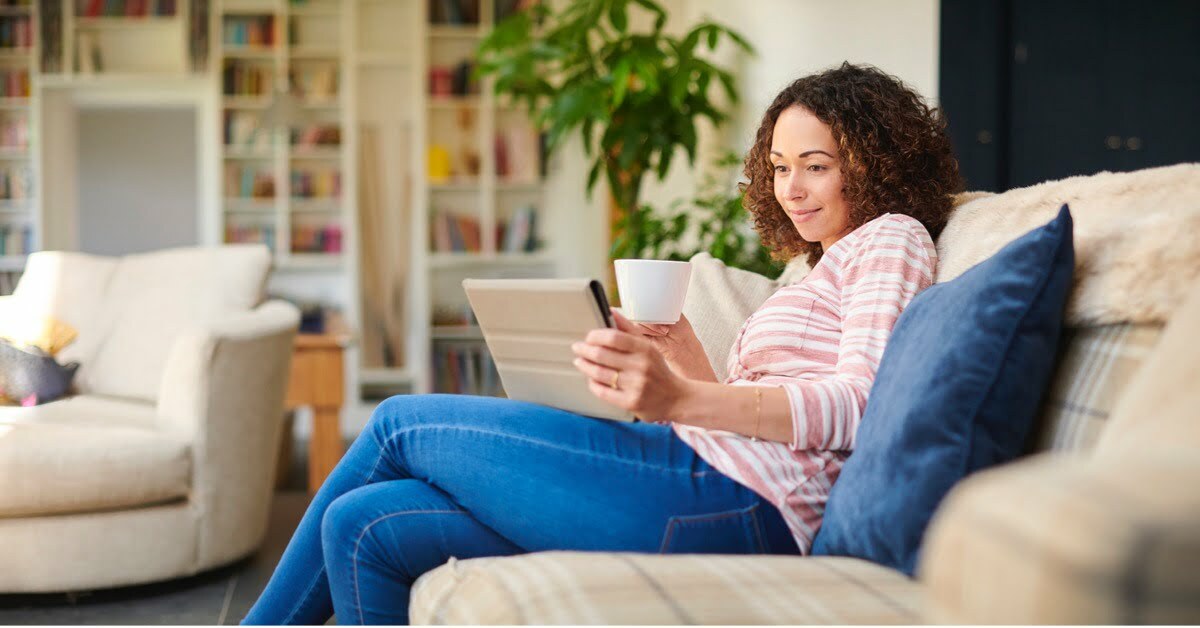 woman on couch watching iPad with tea