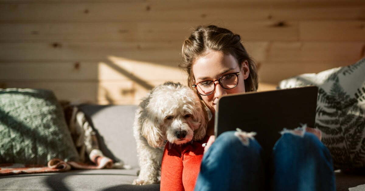 woman and dog sitting on couch looking at tablet