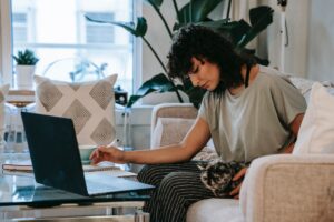 woman and cat on couch in front of laptop
