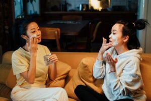 two women applying face masks on couch