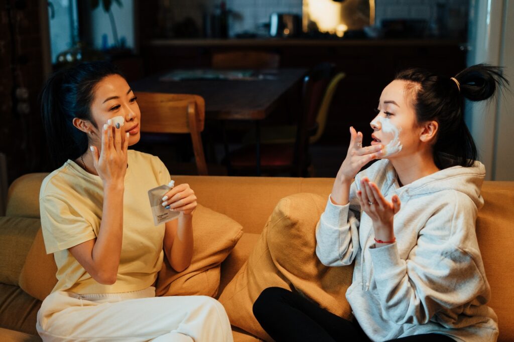 two women applying face masks on couch