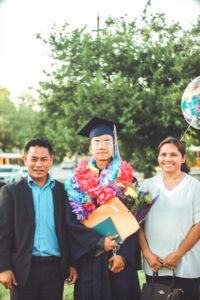 graduate with diploma standing with parents
