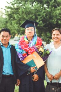 graduate with diploma standing with parents