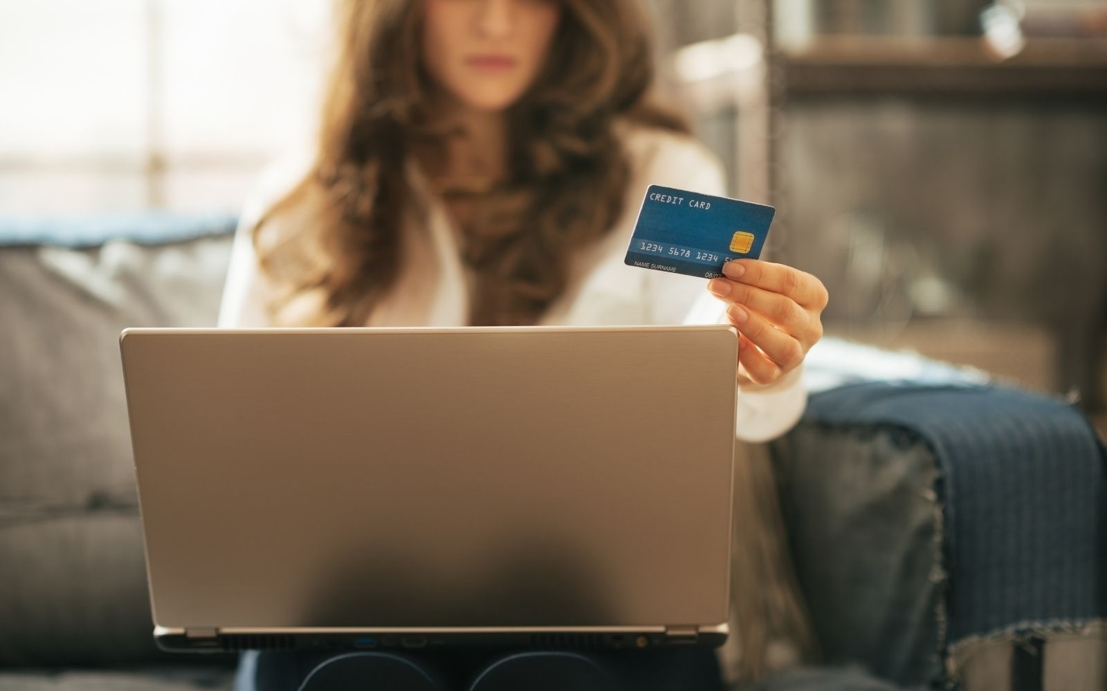 Woman holding a credit card while using a laptop to pay rent online.