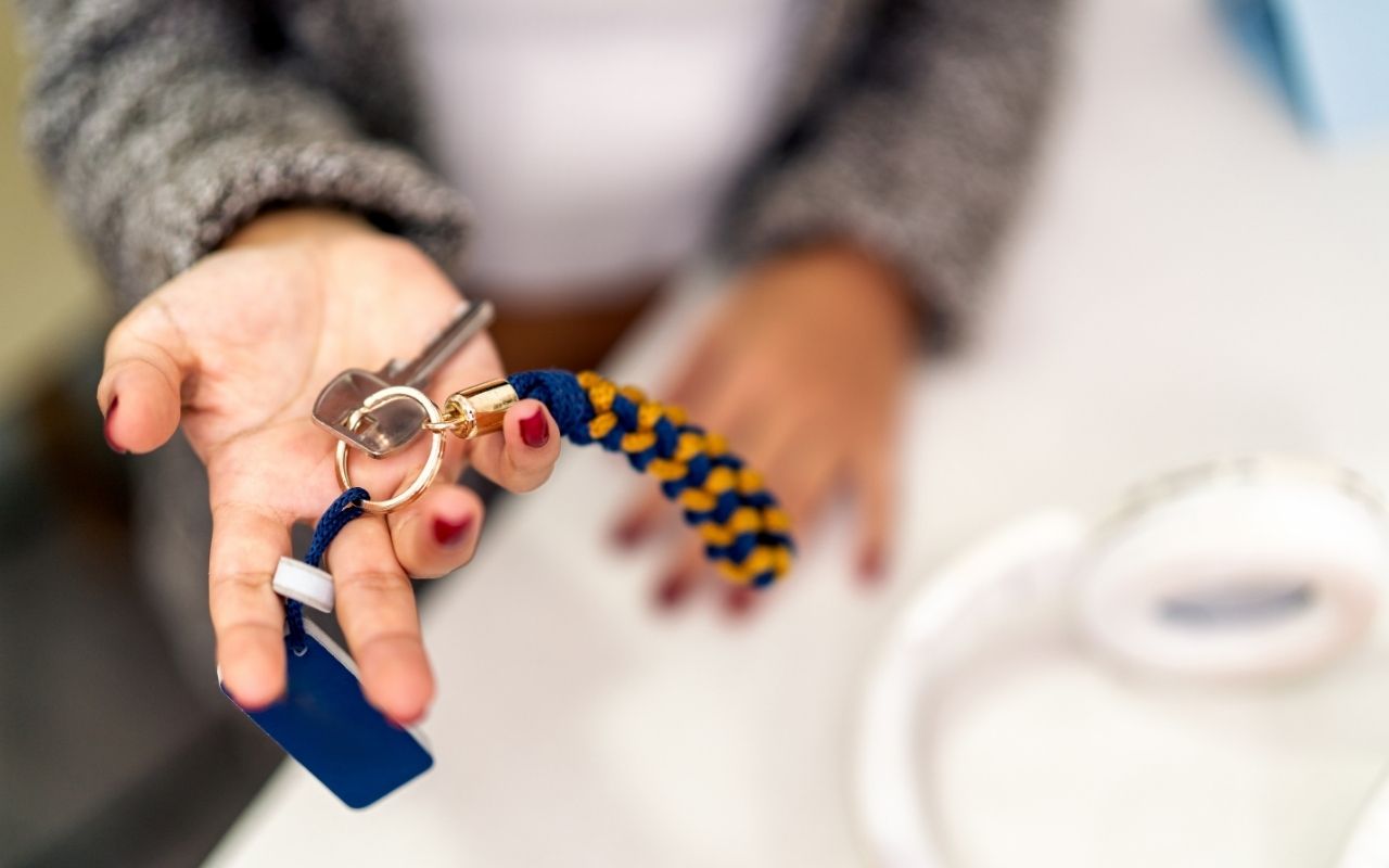 A close-up, first-person perspective of a hand holding out a set of apartment keys with a blue and yellow braided keychain.
