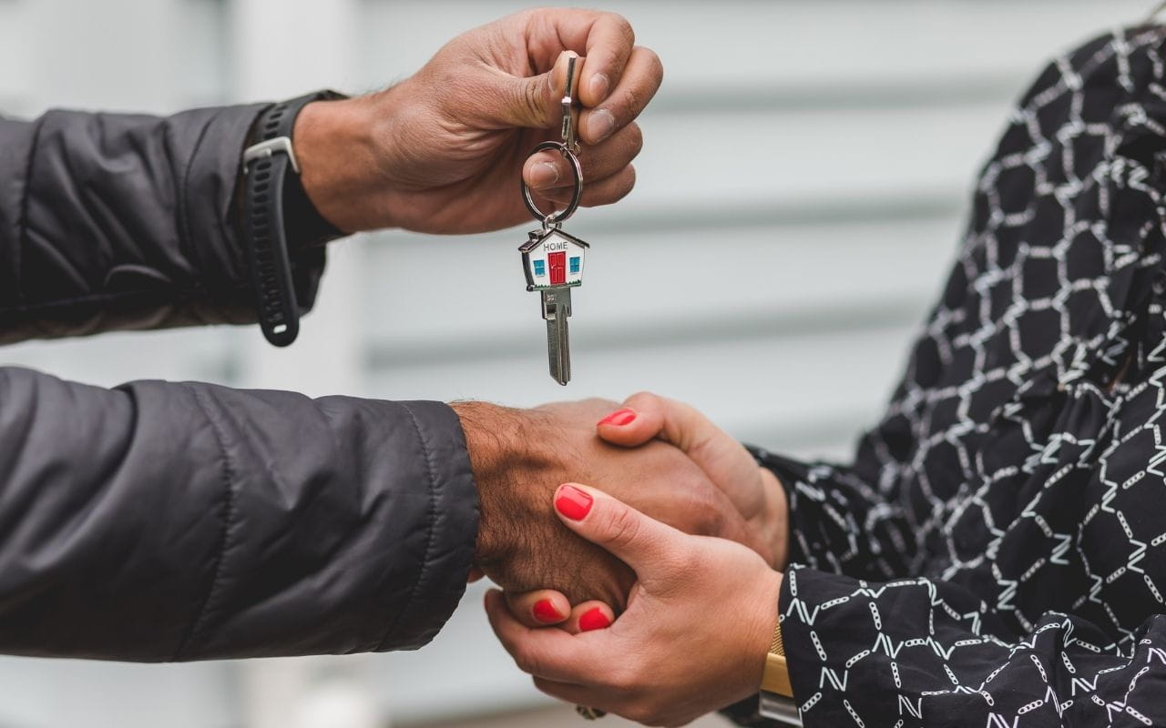 Two people shaking hands while exchanging a house key, representing a homesharing lease agreement